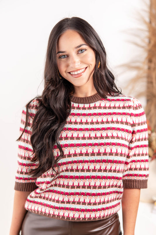 A woman wearing a knit sweater with a hot pink, brown, and cream geometric pattern.
