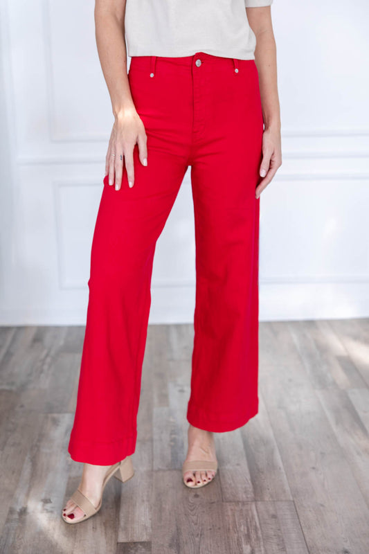 A woman wearing bright red wide-leg cropped pants with a white top and nude heeled sandals.