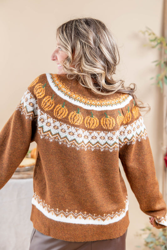 A woman shown from the back wearing a brown knit sweater with a white and orange Fair Isle pattern featuring pumpkins across the shoulders and a geometric border at the hem.