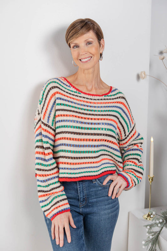 A woman wearing a colorful, long-sleeve striped knit sweater and blue jeans.