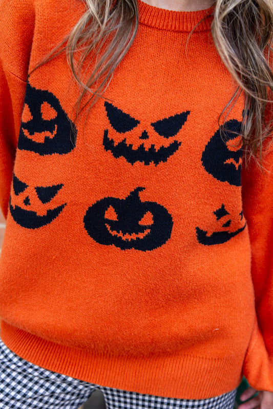 Close up of an orange knit sweater with 6 black jack-o'-lantern graphic.