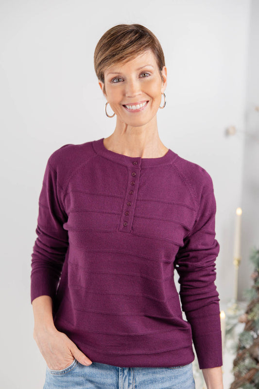 A woman wearing a long-sleeve crewneck sweater in a deep plum purple color, paired with light blue jeans.