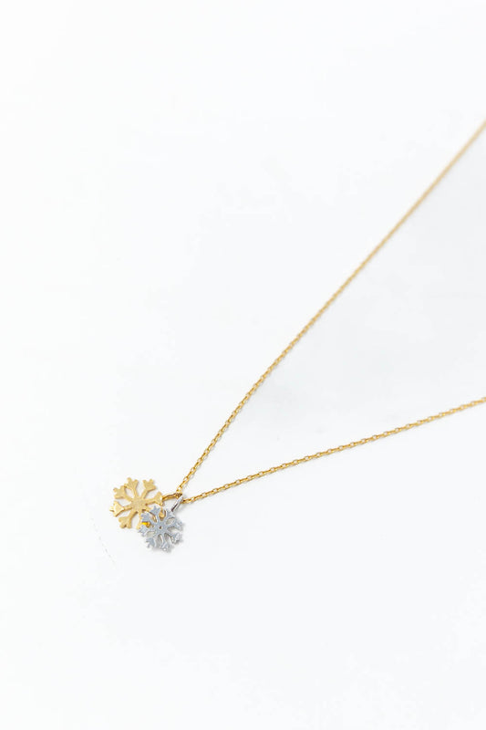 A delicate gold chain necklace featuring two snowflake-shaped pendants, one in yellow gold and one in silver.