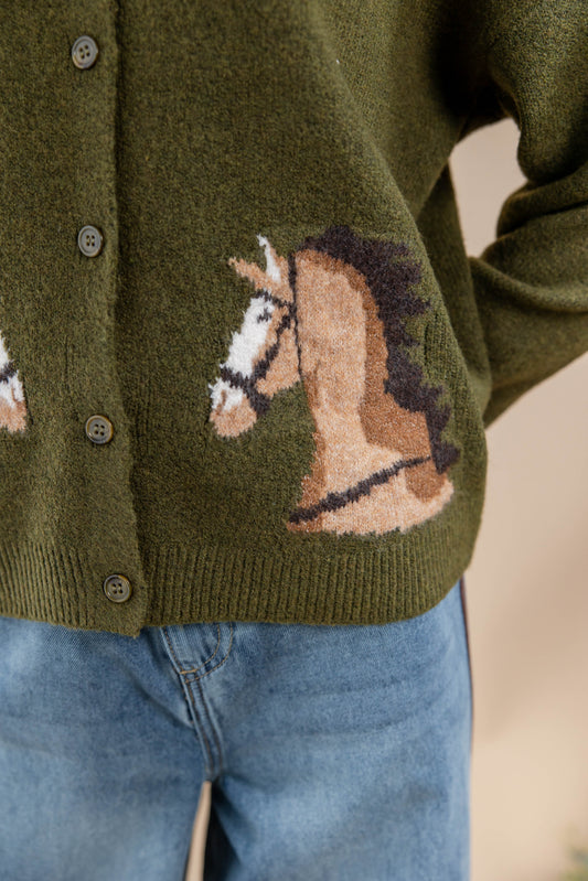 Close-up of an olive green knit cardigan with a horse motif in tan, brown, and black, worn with blue jeans.