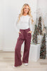 A woman modeling a pair of burgundy wide-leg pinstripe pants with a white long-sleeve top.