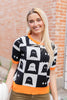 A woman wearing a black and white checkered sweater with orange trim and ghost patterns.