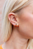 A close-up side profile of a blonde woman wearing a small orange jack-o'-lantern stud earring with black detailing.