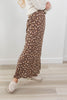 A person wearing a long brown floral maxi skirt with a cream sweater and white loafers, standing on a light wood floor against a white wall.