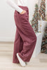 A woman wearing wide-leg maroon trousers with thin white vertical pinstripes, paired with a white long-sleeve top and white slip-on shoes.
