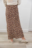 A person wearing a long brown maxi skirt with a dense small floral print in beige and muted orange, paired with a cream sweater and cream loafers, standing on a light wood floor against a white wall.