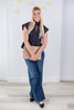 A woman stands in a bright room wearing a black cap sleeve keyhole button-front top, blue wide-leg jeans, and black heels, while holding a clipboard.