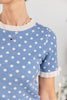 Close-up of a woman wearing a light blue short-sleeve knit top with white polka dots and white ruffled trim at the collar and sleeve cuffs.