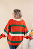 A woman wearing a ribbed knit sweater with horizontal orange, green, and white stripes, shown from the back in a warm indoor setting.
