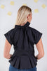 A woman viewed from behind wearing a black short-sleeve blouse with a large bow at the back of the neck and a peplum waist, paired with blue jeans against a light gray wall.