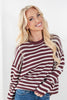 A smiling blonde woman wearing a maroon and cream striped knit sweater with blue jeans, photographed against a clean white background.