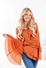 A woman wearing a rust orange long-sleeve blouse with a V-neck and tiered bell sleeve flared cuffs.