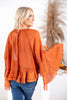 A woman from behind wearing rust orange long-sleeve blouse with a ruffle hem and tiered bell sleeve flared cuffs.
