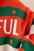 Close-up of a knitted sweater with horizontal orange, green, and white stripes, featuring a small orange maple leaf motif and partial white lettering.