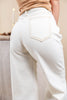 Close-up back view of a woman wearing off-white wide-leg jeans with contrast stitching and a V-shaped back pocket detail, paired with a tan top.