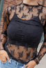 A woman wearing a black sheer lace long-sleeve top over a black ribbed camisole, paired with blue jeans and a halloween necklace.