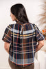 Woman wearing plaid top with navy, white, orange, and blue stripes, featuring a brown faux-leather collar trim from behind.