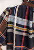 Close up of a woman wearing a plaid top with navy, white, orange, and blue stripes, featuring a brown faux-leather collar trim.