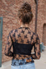A woman from behind wearing a black sheer lace long-sleeve top over a black ribbed camisole, paired with blue jeans.