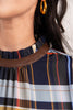 Close-up of a woman wearing a plaid top with navy, white, orange, and blue stripes, featuring a brown faux-leather collar trim.