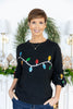 A woman wearing a black crewneck sweater with a colorful Christmas light bulb pattern across the chest and sleeves, paired with blue pinstripe jeans.