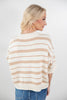 A woman shown from the back wearing a cream knit sweater with thin tan horizontal stripes and blue jeans, photographed against a light gray studio background.