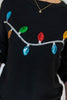 A close-up of a black knit sweater featuring a sequined Christmas light string design across the chest, with colorful bulbs in blue, green, red, orange, and yellow on a silver wire.