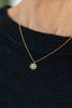 A close-up of a person wearing a delicate gold chain necklace with a small snowflake-shaped pendant set with clear stones, paired with a black knit sweater.