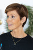 A woman, wearing a black knit sweater, a delicate snowflake gold necklace, and a gold stud earring.