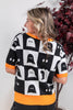 A woman wearing a black and white checkered sweater with ghost patterns and bright orange trim, shown from the back in an indoor setting.