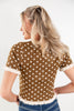 A woman shown from the back wearing a brown short-sleeve top with white polka dots and cream ruffled trim, paired with blue jeans, against a plain white background.