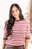 A woman wearing a knit sweater with a hot pink, brown, and cream geometric pattern.
