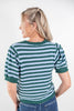 A woman shown from the back wearing a green and light blue striped knit top with short puff sleeves and a scalloped hem, paired with blue jeans, against a plain white studio background.
