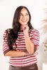 A woman wearing a red, brown, and cream patterned knit short sleeve sweater.