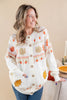 A woman wearing a cream-colored button-up cardigan with autumn-themed knit patterns including turkeys, acorns, and leaves, paired with blue jeans in a warm indoor setting.