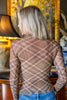 A woman viewed from behind wearing a sheer brown mesh long-sleeve top with a beige diagonal plaid pattern, paired with blue jeans in an indoor setting.