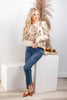 A woman models a cream-colored knit sweater with an orange and green floral pattern, paired with blue jeans and brown flats.