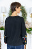 A woman shown from the back wearing a black knit sweater with colorful Christmas light bulb patches on the sleeves, paired with blue pinstripe pants.