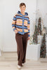 A woman wearing a multicolor striped knit cardigan with a hood and brown wide-leg pants. The cardigan has horizontal stripes in blue, pink, yellow, and brown, with a blue front panel and buttons.