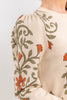 Close-up of a cream-colored knit sweater featuring orange embroidered flowers and olive green leafy vines on the sleeve and chest.
