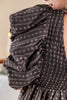 Close-up of a dark brown smocked dress with voluminous puffed sleeves and a delicate white floral pattern, worn by a model.