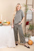 A woman modeling a matching two-piece houndstooth jumpsuit set in a cozy, autumn-themed indoor setting with pumpkins, a table, and a ladder backdrop.
