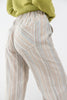 Close-up of a person wearing blue and tan striped trousers with back pockets and a light olive green sweater draped off the shoulders, against a plain light background.