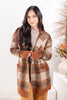 A woman wearing a long open-front knit cardigan with a brown, beige, and gray plaid pattern, styled over a beige turtleneck sweater and tan pants.