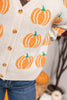 A close-up of a person wearing a cream knit cardigan with orange pumpkin patterns and wooden buttons, paired with blue jeans.