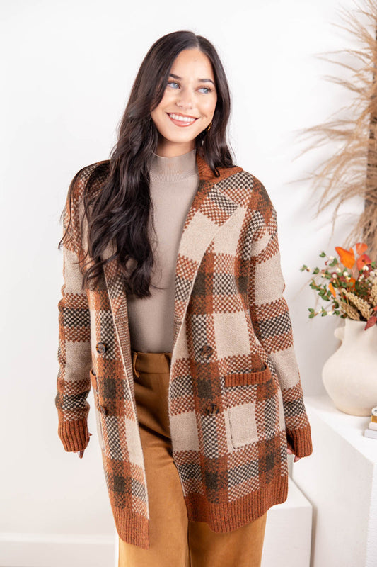 A woman wearing a brown and beige plaid knit cardigan over a taupe turtleneck and brown pants.